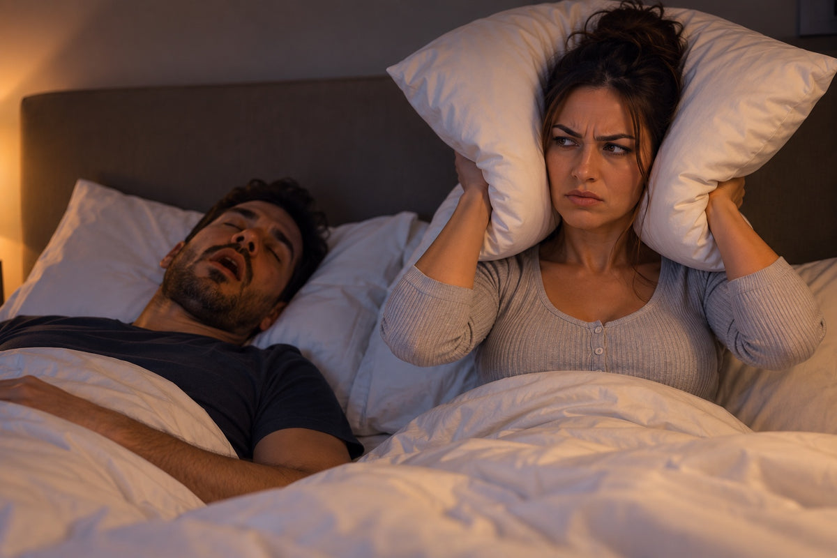 A woman holding a pillow over her ears beside her sleeping partner